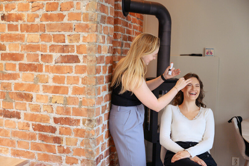 Hair stylist and make-up artist is putting make-up on a happy model