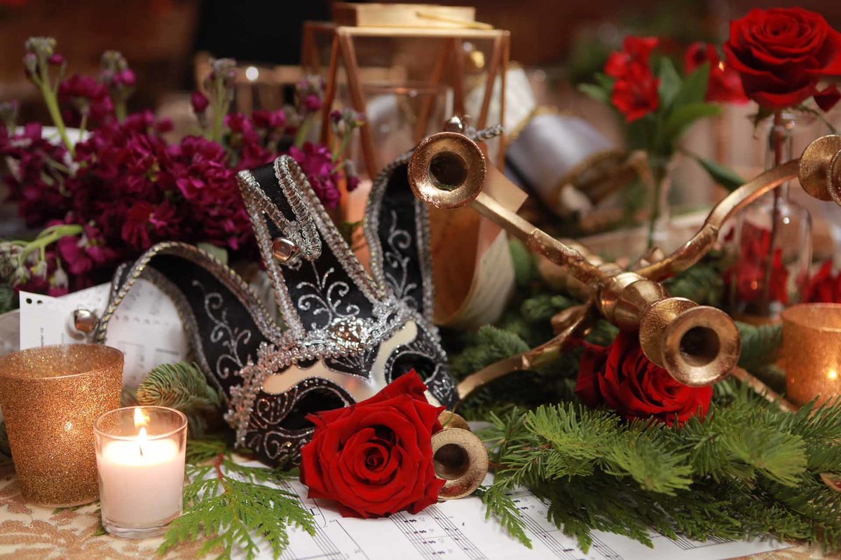 holiday centerpiece with gold centerpiece, carnival mask, evergreen, red roses, gold candelabras