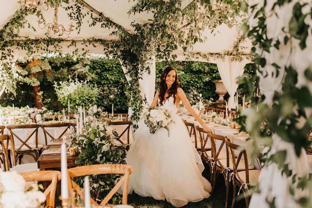 a happy bride in her wedding reception tent covered in smilax greenery, long tables with Vineyard chairs