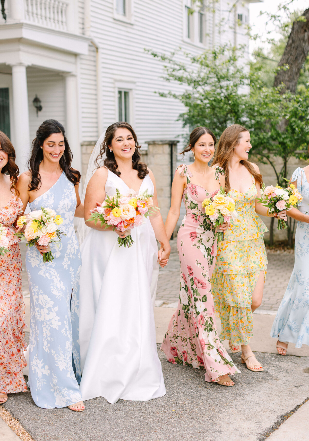 Bride and bridesmaids with flawless hair and makeup walking outdoors, styled by Austin wedding beauty team Mistique Makeup for a spring ceremony