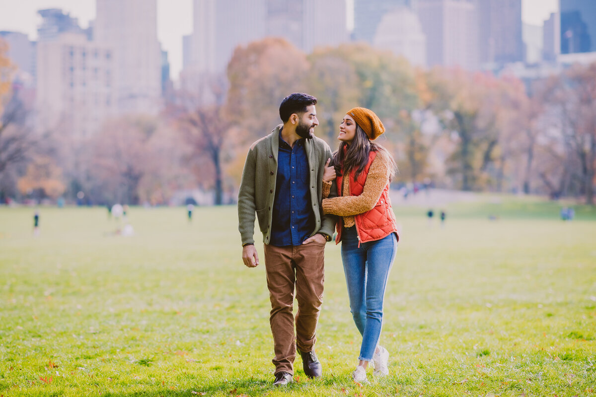 Engaged couple walking through the central park lawn in fall clothing in autumn
