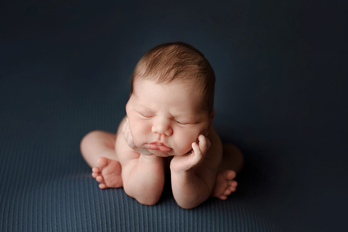 Newborn holding its face in hands posed for newborn portrait