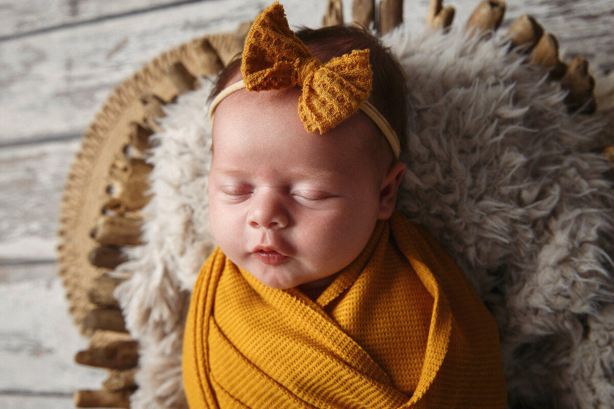 Close-up portrait of baby girl wrapped in an orange blanket with an orange bow on her head