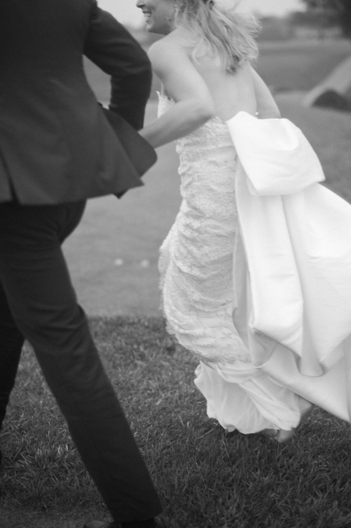 The bride and groom run hand in hand across the grass