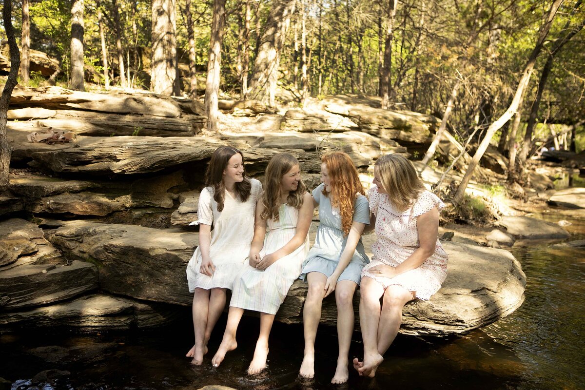 The three sisters sitting together by the creek in Flower Mound, enjoying a peaceful moment while posing for their photoshoot