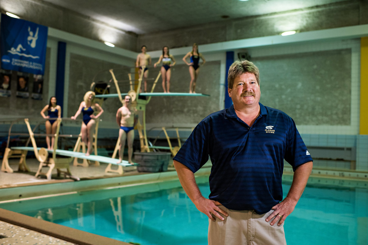 A college swim coach with his students behind him on diving boards.