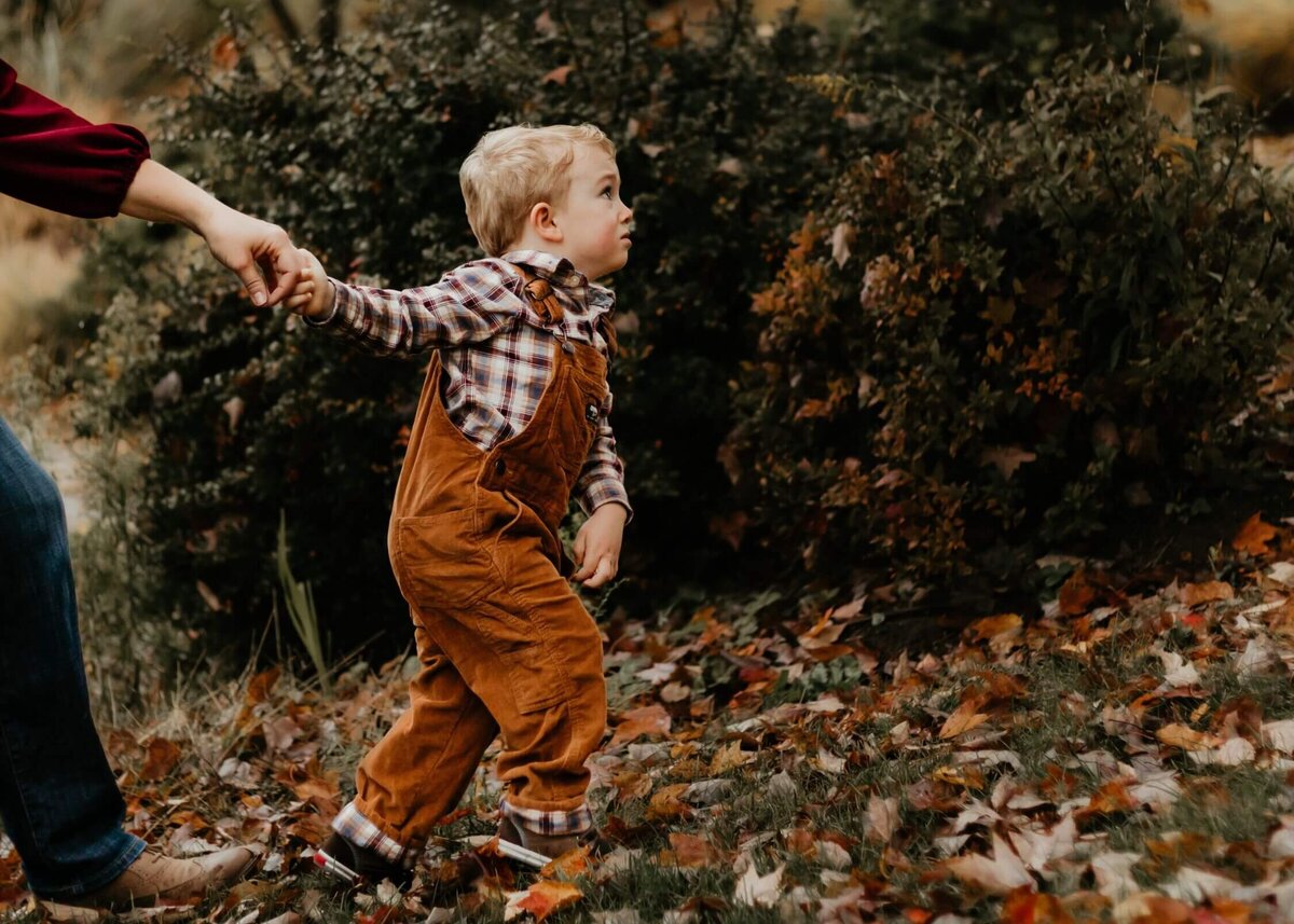 A woman and her son walking through the leaves in a park captured by a Pittsburgh family photographer.