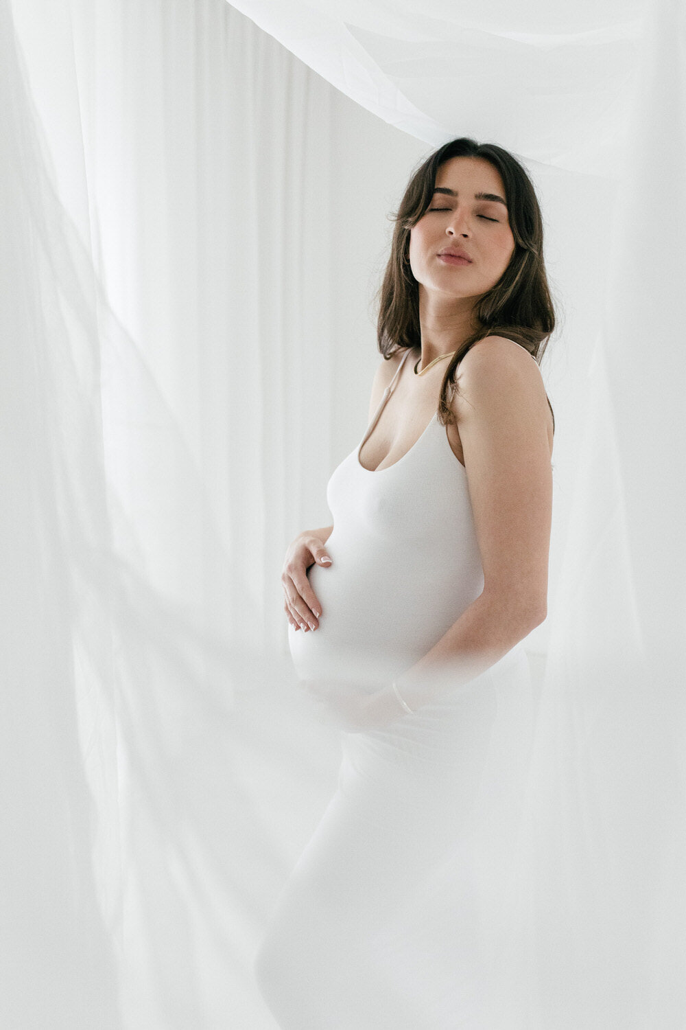 Pregnant women in white studio with eyes closed holding her belly