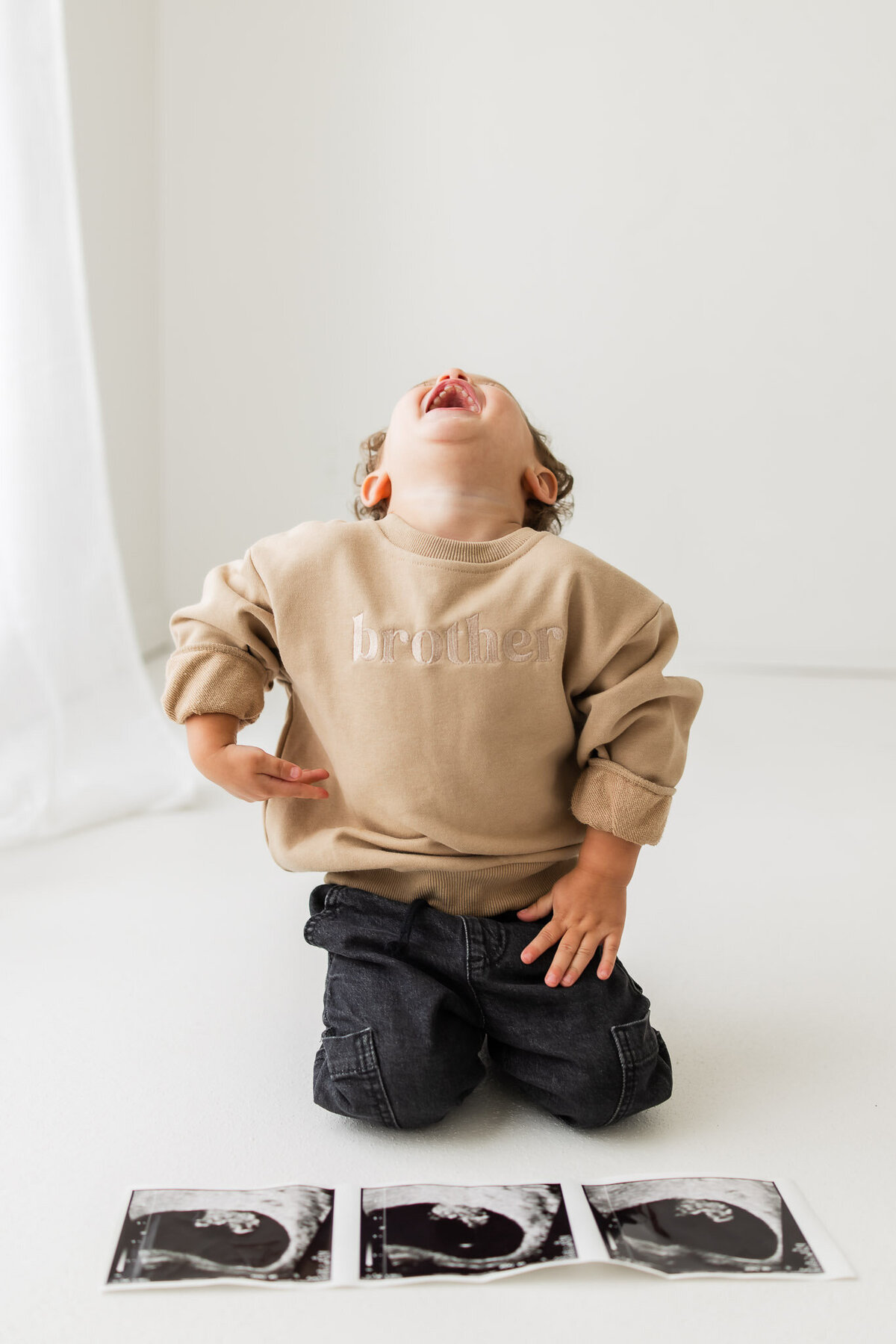 Little boy with an ultrasound photo of his baby sibling in front of him, he is laughing with his head back