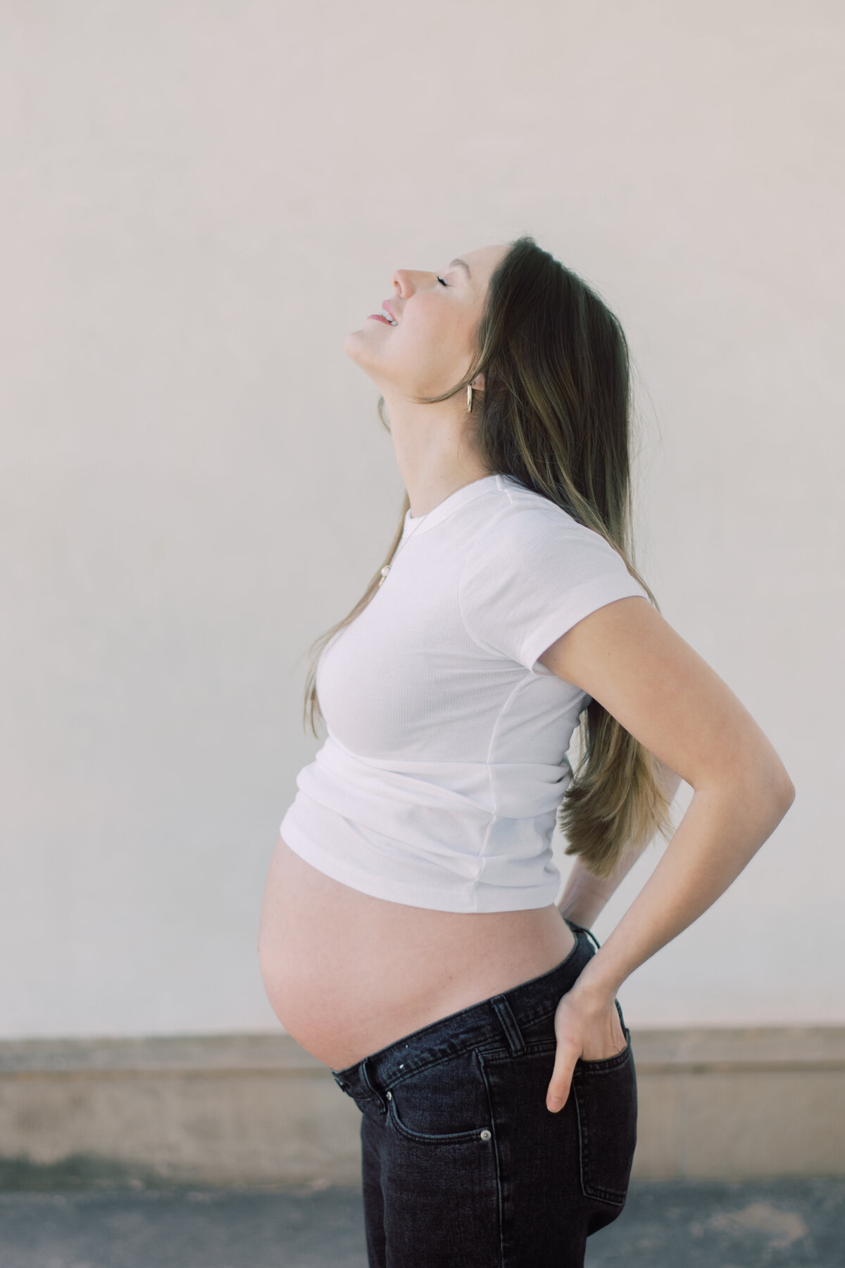 Softly lit color image of a pregnant woman embracing her belly, styled in all-white Zara pieces
