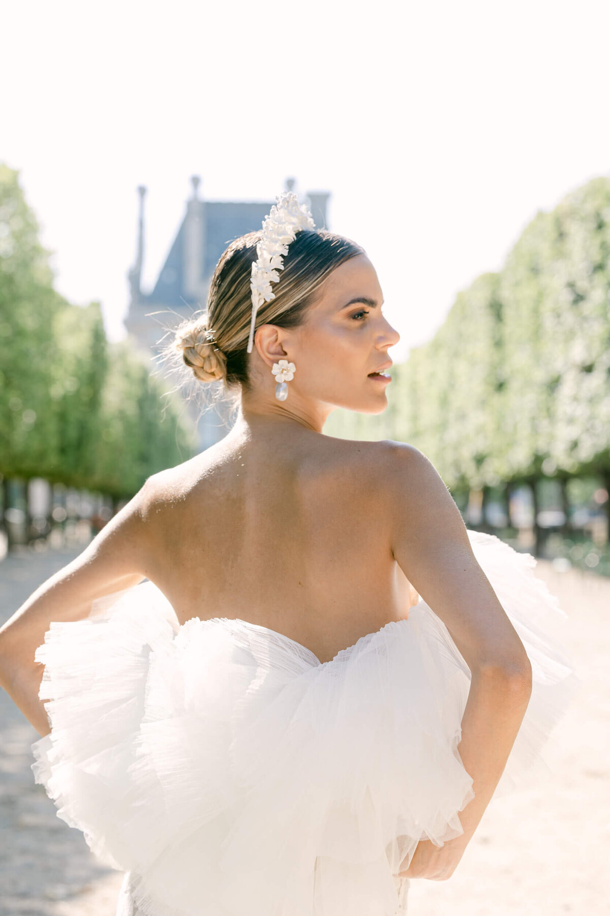 a picture of a bride in her whte dress and white floral head piece in paris surronded by trees with a chateau in the background