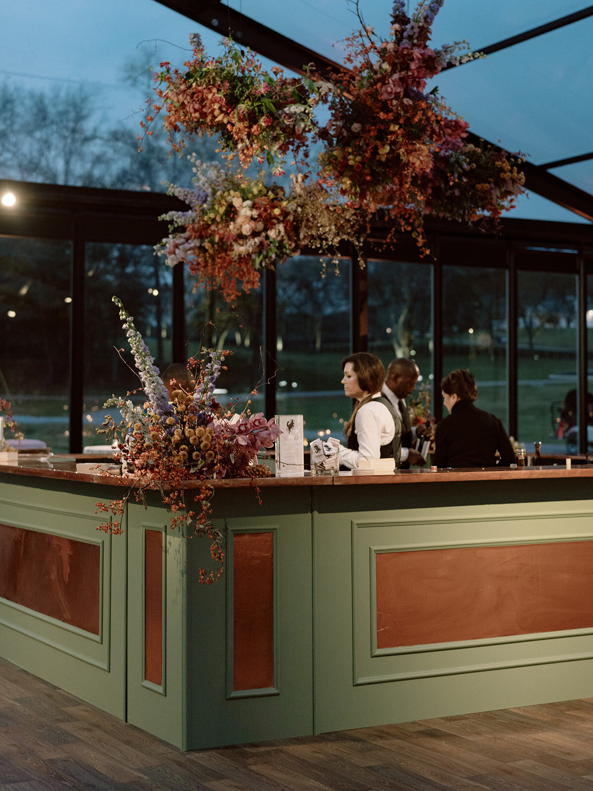 Interacting and sculptural floral clouds hang over the dance floor and bars of this fall wedding reception in Tennessee. Clear top tent build out for fall wedding reception in Tennessee hills.  Product clustered floral clouds in a tasteful fall color palette of copper, ruby, gold, burgundy, rust, and lavender. Orchids, bittersweet berries, butterfly ranunculus, and tulips are highlighted. Unique floral design with flower forward large scale installations. Design by Rosemary & Finch Floral Design in Nashville, TN.