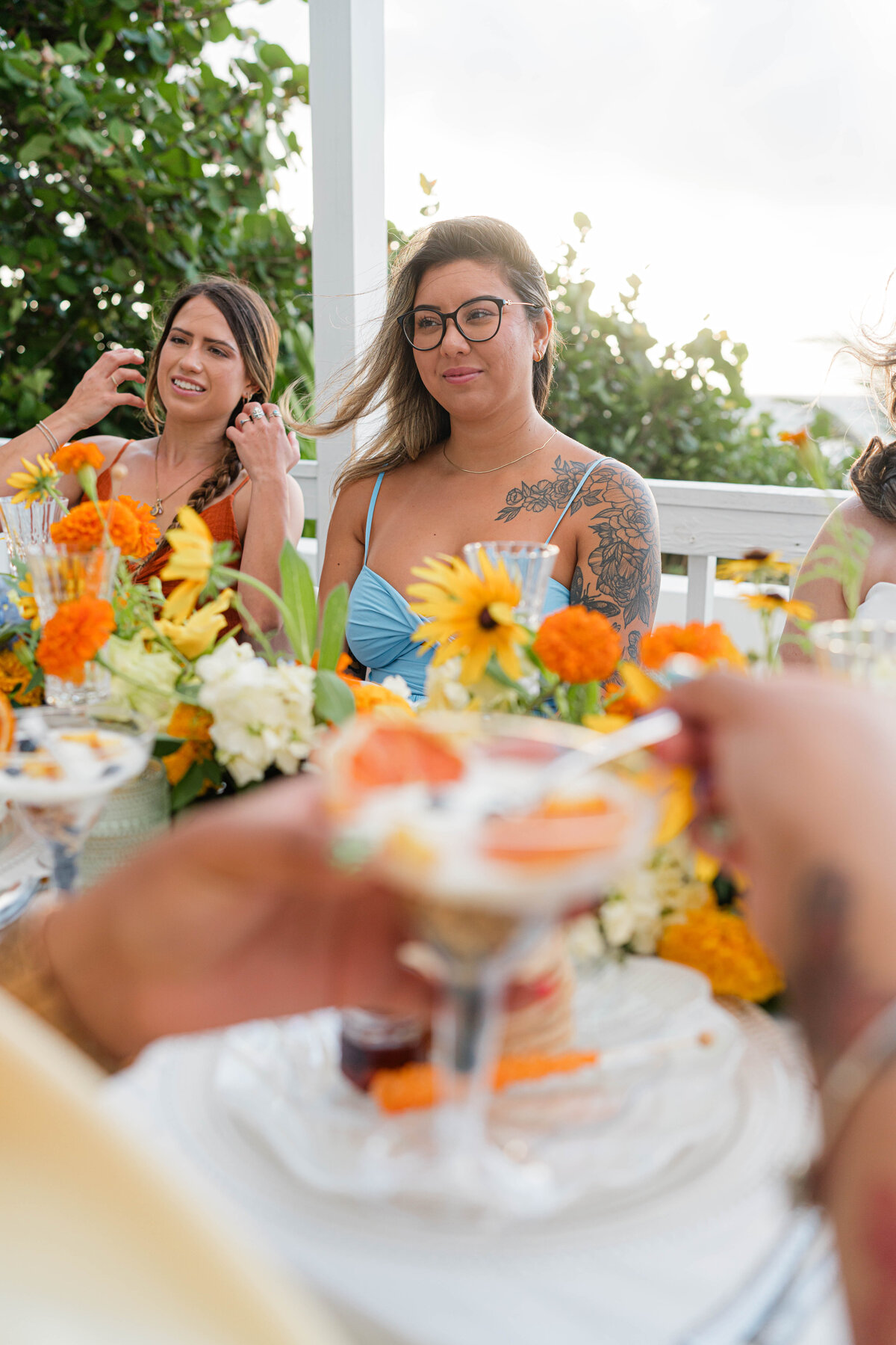girlfriends at beach brunch the table is adorned with white, orange, blue and green floral table runner and fruit parfaits in martini glasses
