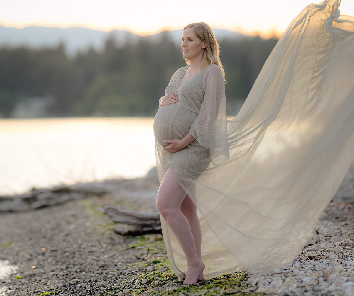 A mom-to-be in a sheer golden dress, her fabric flowing in the wind, creates a stunning and serene image by Beth Benecki.