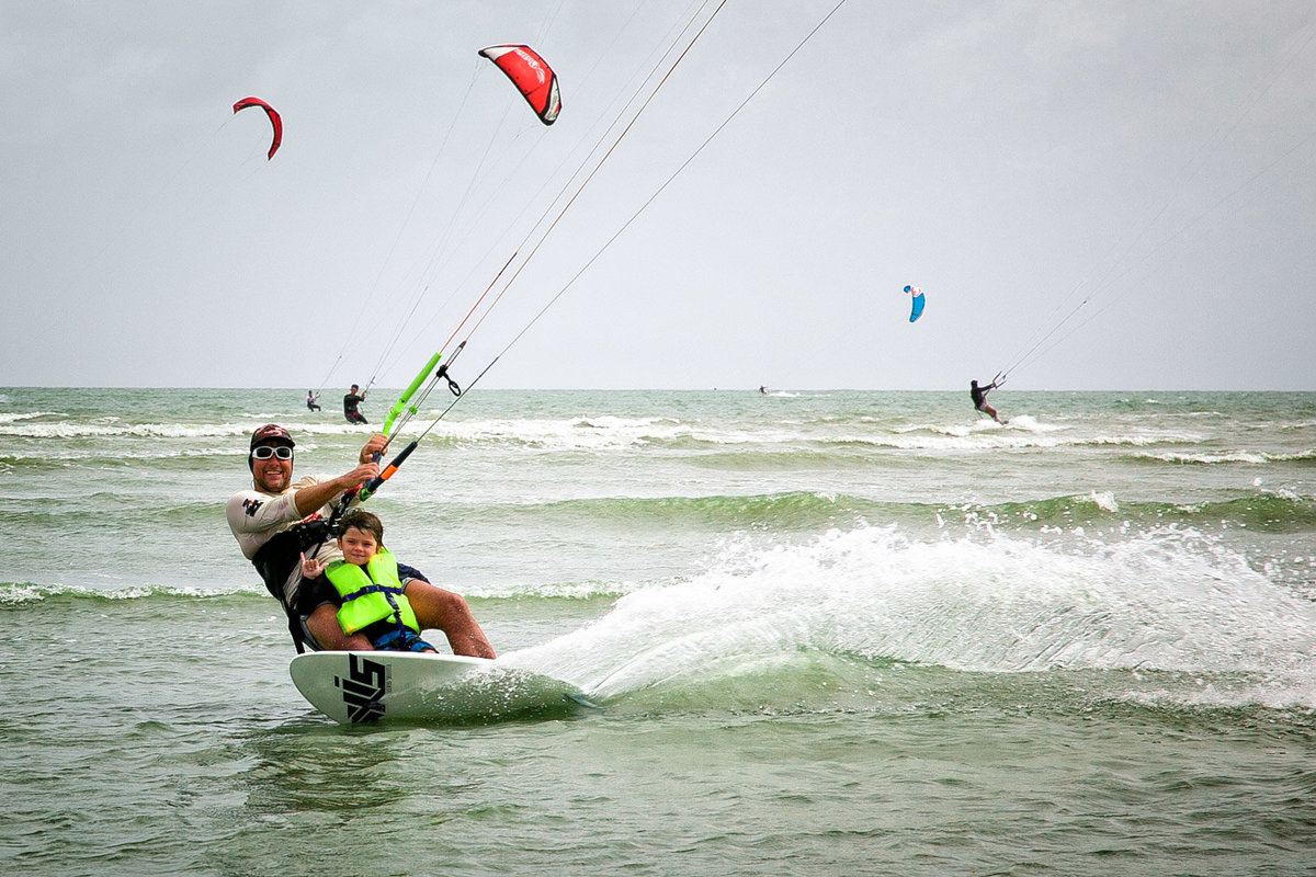 A father and son kite surf leaving a dramatic wake behind them. Photo by Ross Photography, Trinidad, W.I..