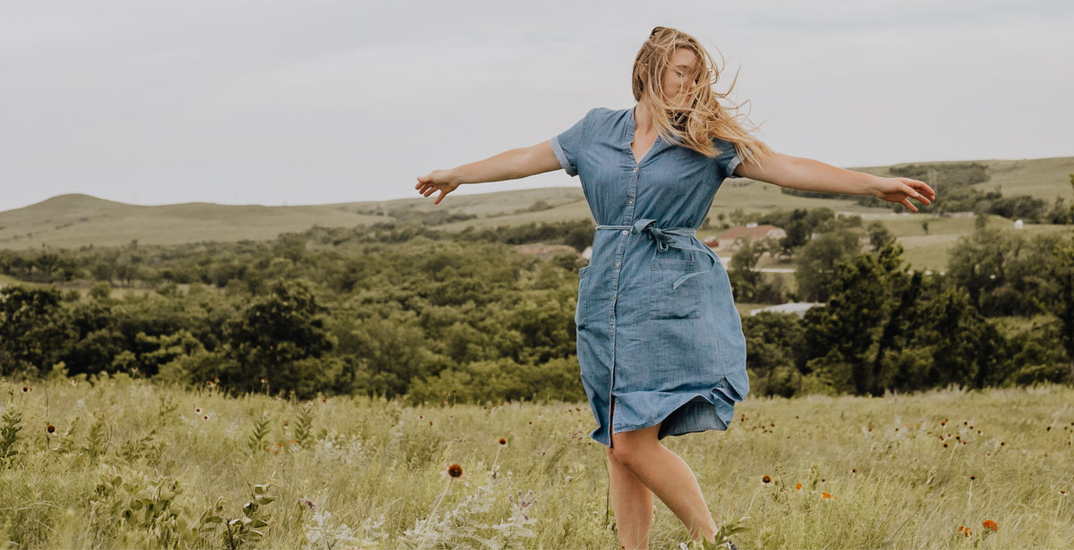 Girl in blue dress, arms out and wind blown hair on top of a mountain.