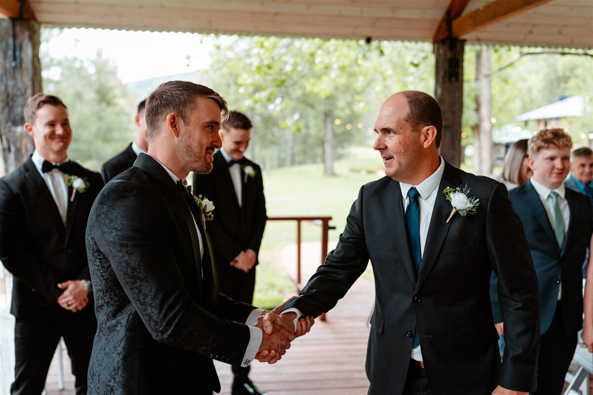 The groom firmly grasps his father-in-law's hand, sealing a bond of respect and kinship.