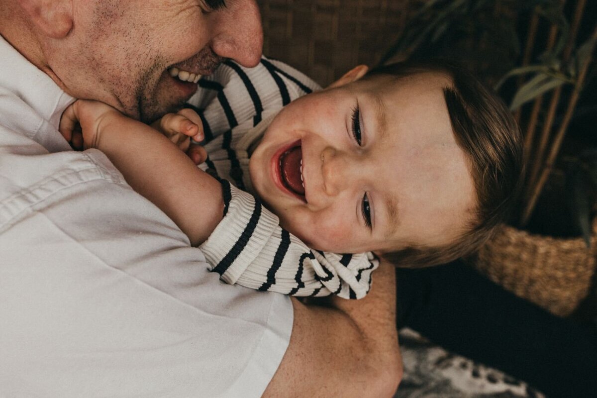 A joyful close-up of a father laughing while holding his happy baby close to his chest. A heartwarming and candid family moment