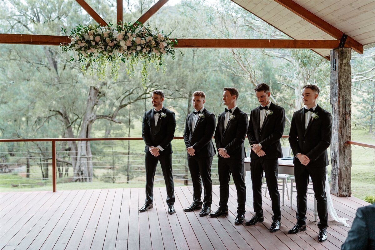 A groom, surrounded by his eager friends, awaits the arrival of his bride with joyful anticipation.