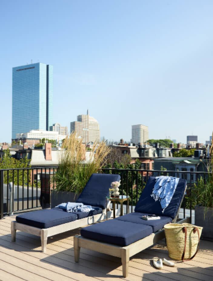 Interior Designers in Boston designed a brownstone roof deck with navy blue cushions, chaise lounges, and views of the Back Bay.