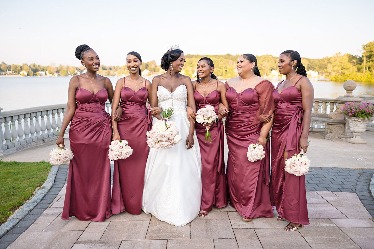 Bride in a white gown smiling with her bridesmaids in matching burgundy dresses