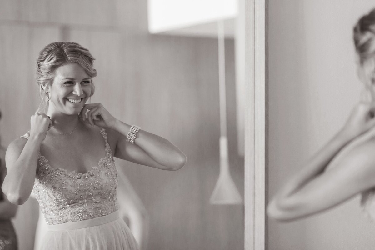 Bride looking in mirror adjusting necklace before wedding.