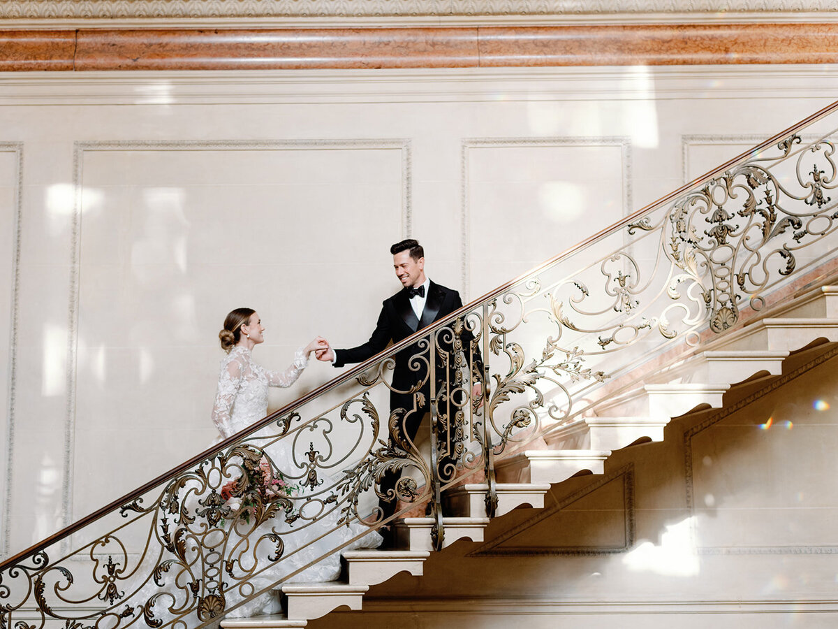 A groom looking towards his bride and they walk up the steps in Larz Anderso House as the beautiful sunlight reflects them.