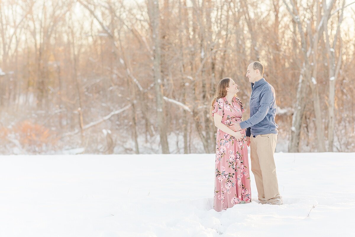 couple looks at eachother during snowy winter maternity photo session with Sara Sniderman Photography in Medfield Massachusetts