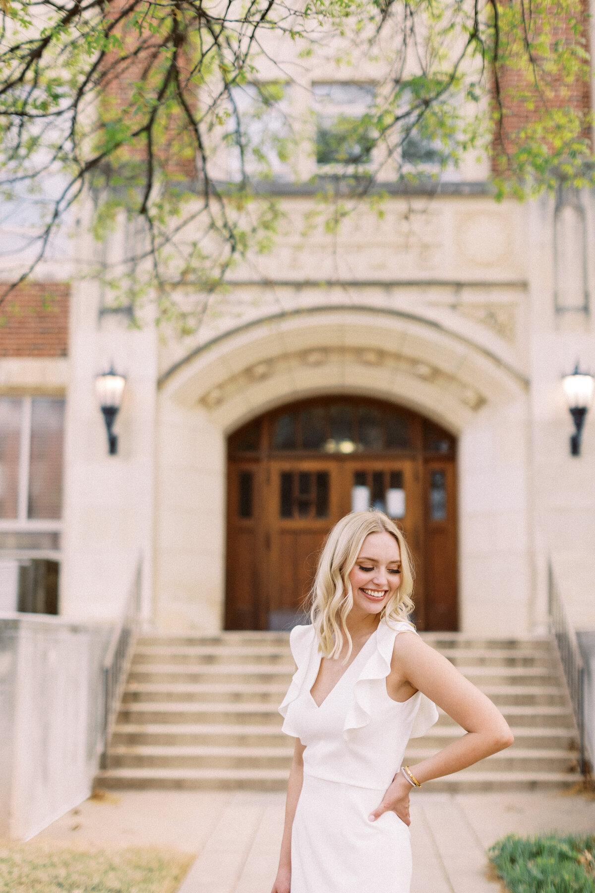 young woman poses confidently in front of college building at the university of oklahoma