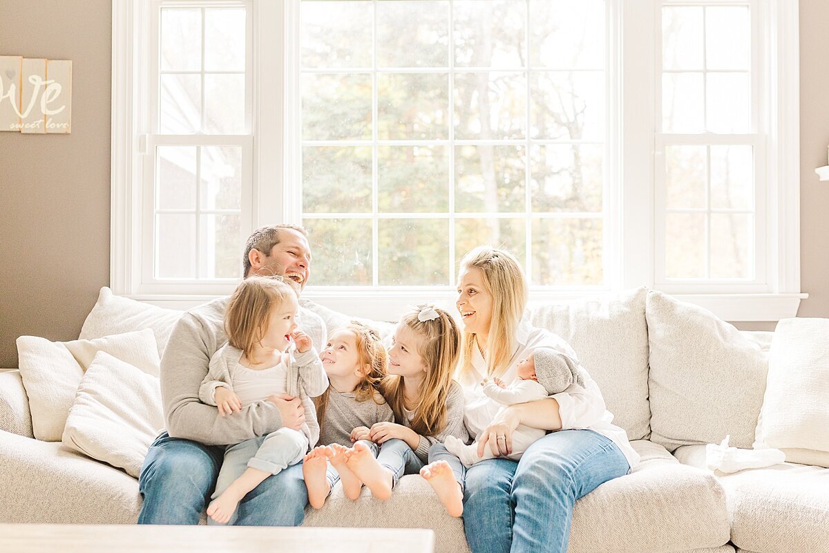 family sits on couch  during in home newborn photo session with Sara Sniderman Photography in Sherborn Massachusetts