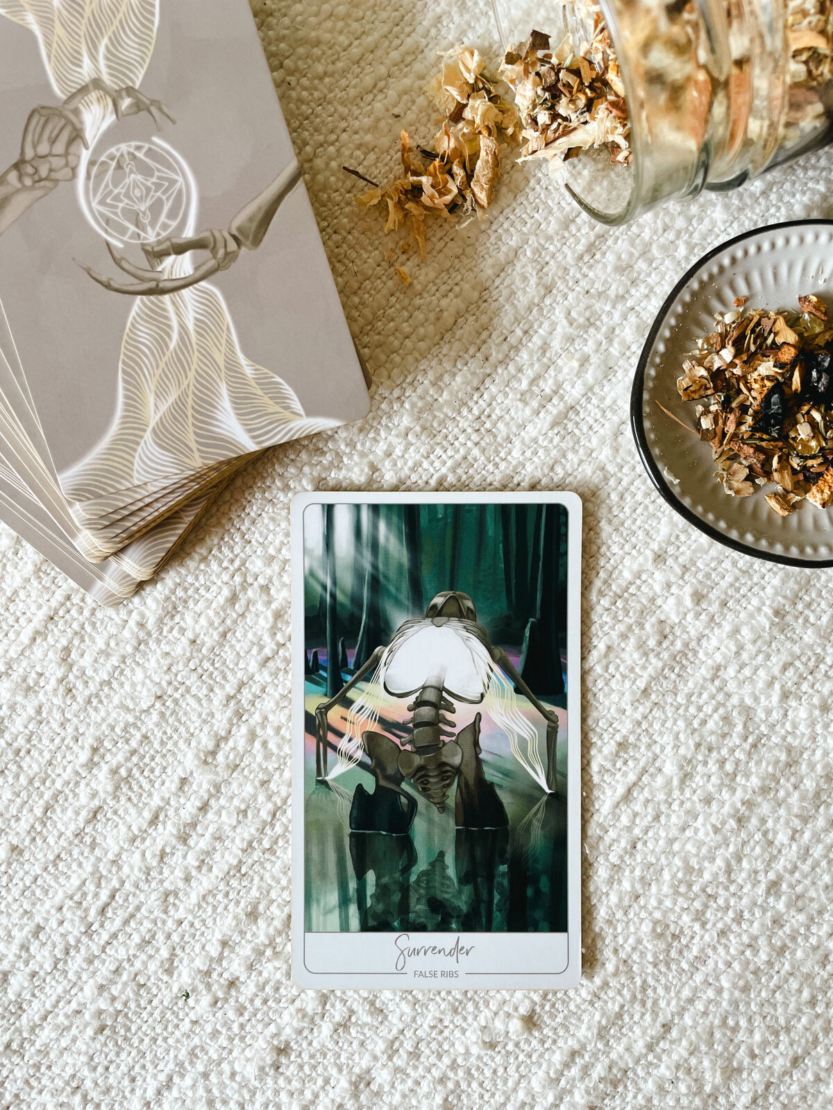 Close up of the "Surrender" Oracle Card which corresponds to False Ribs in your anatomy and shows a skeleton in a swamp with light radiating from the chest