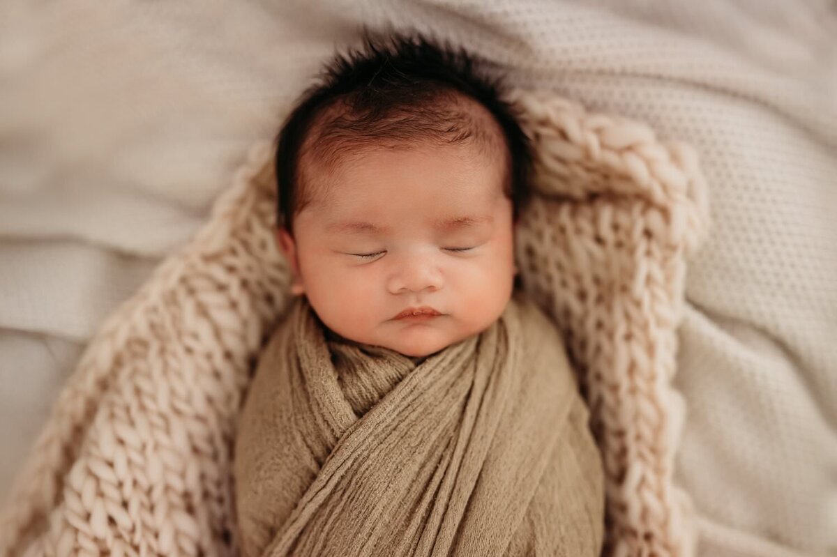 newborn baby boy in a cozy tan wrap in a photography studio session