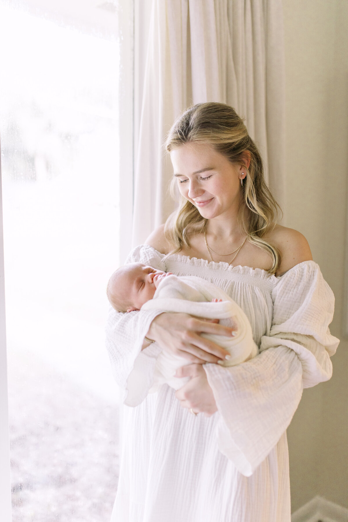 newborn portrait taken in home in Jacksonville with mom in a creamy white dress gazing lovingly at her newborn baby boy