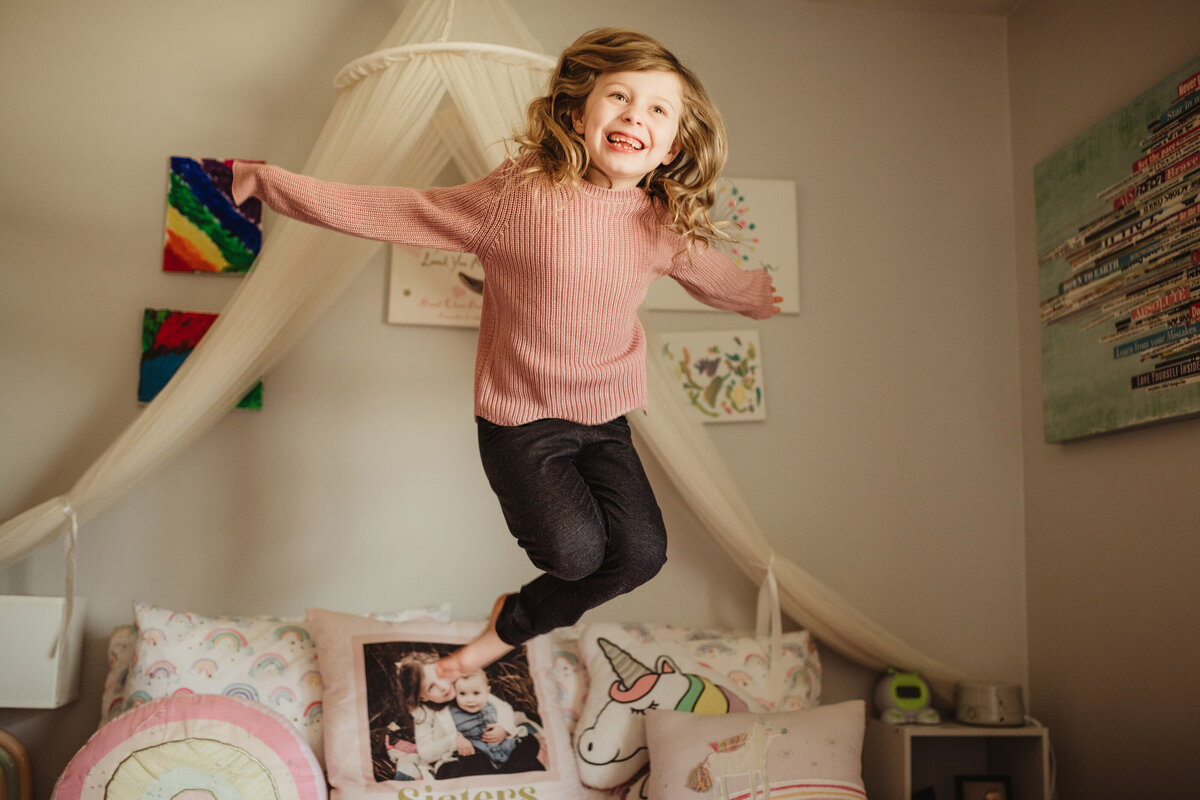 A young girl jumps high on her unicorn-themed bed.