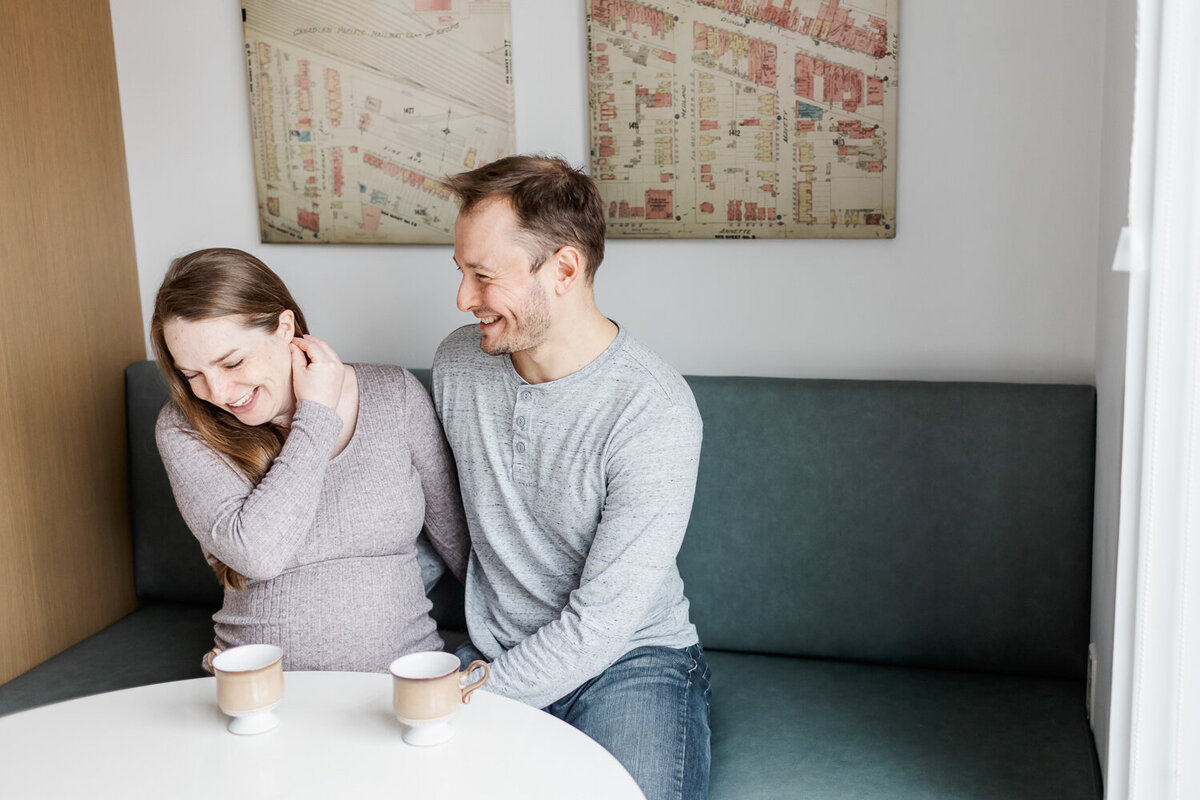 Expecting couple sitting in kitchen having a laugh during their toronto maternity photography session by Claire Binks Photography