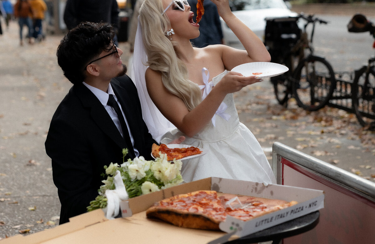 Bride and groom toasting their pizza slices together in celebration of their NYC elopement.