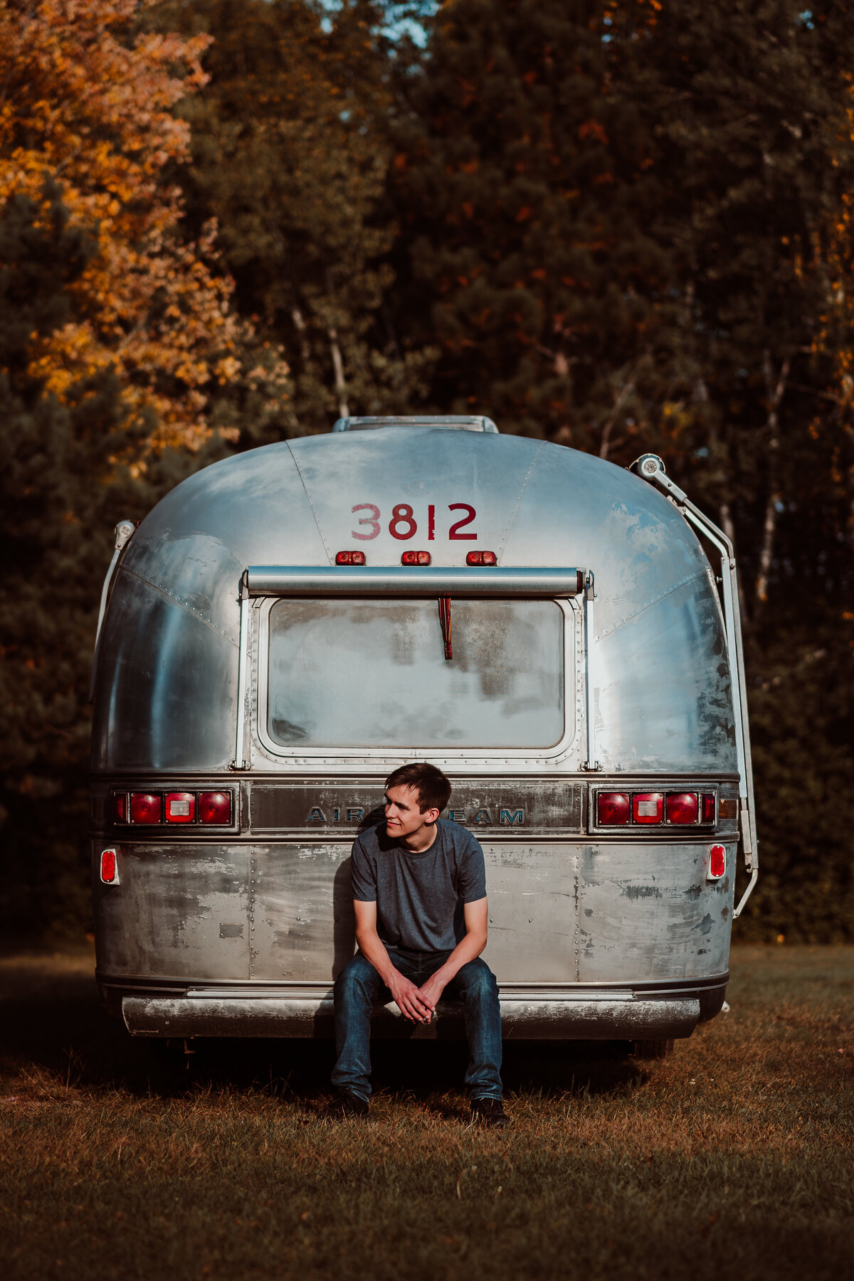 Outdoor portrait of male senior in Minnesota sitting on an Airstream outside.
