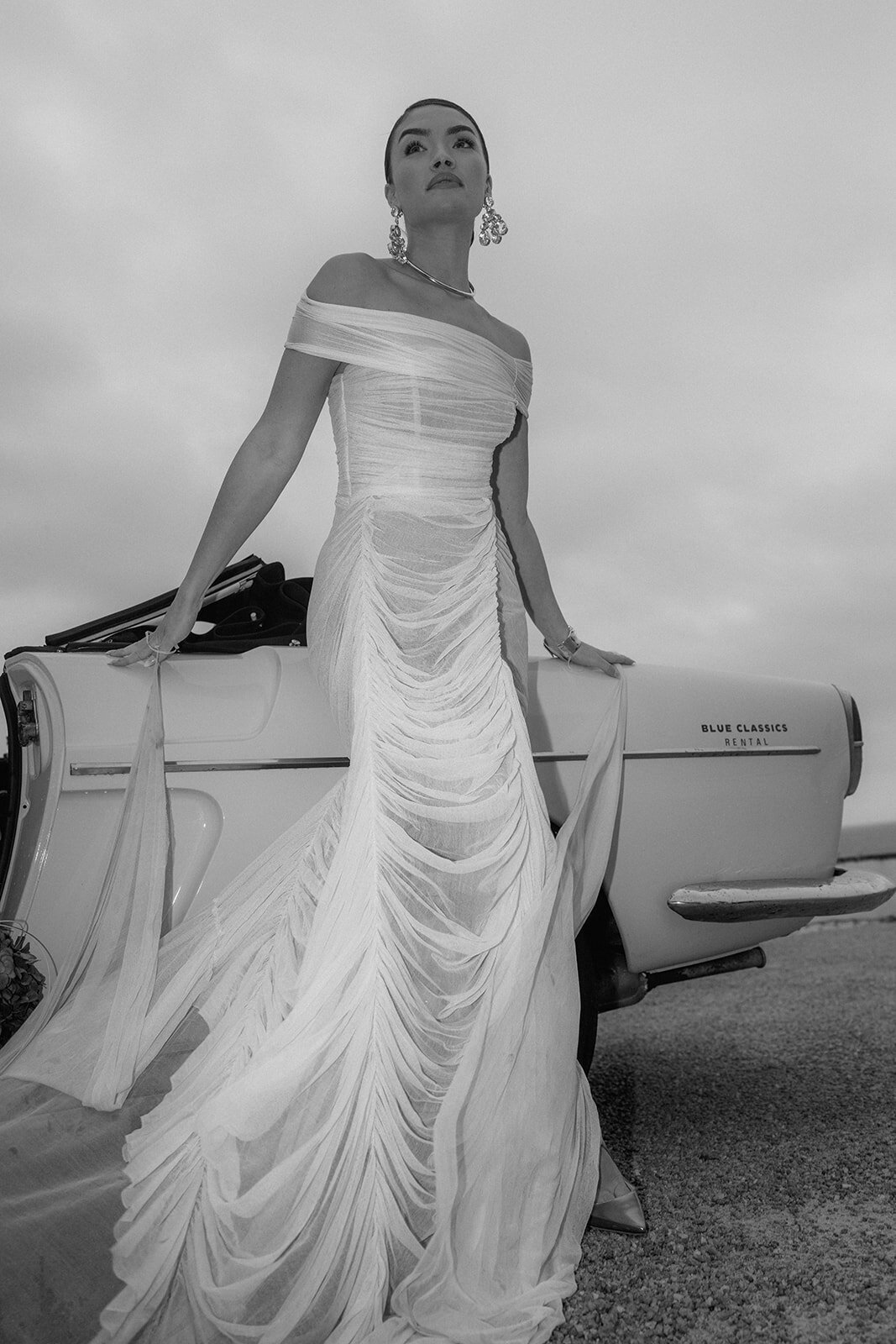 Bride poses leaning at a vintage car during wedding session.