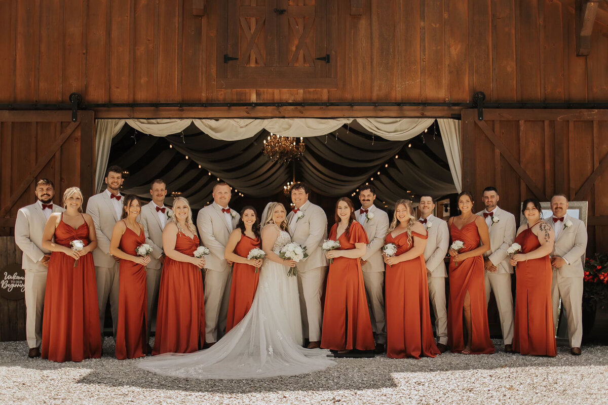 Wedding party posing in front of the barn with bridesmaids in orange dresses