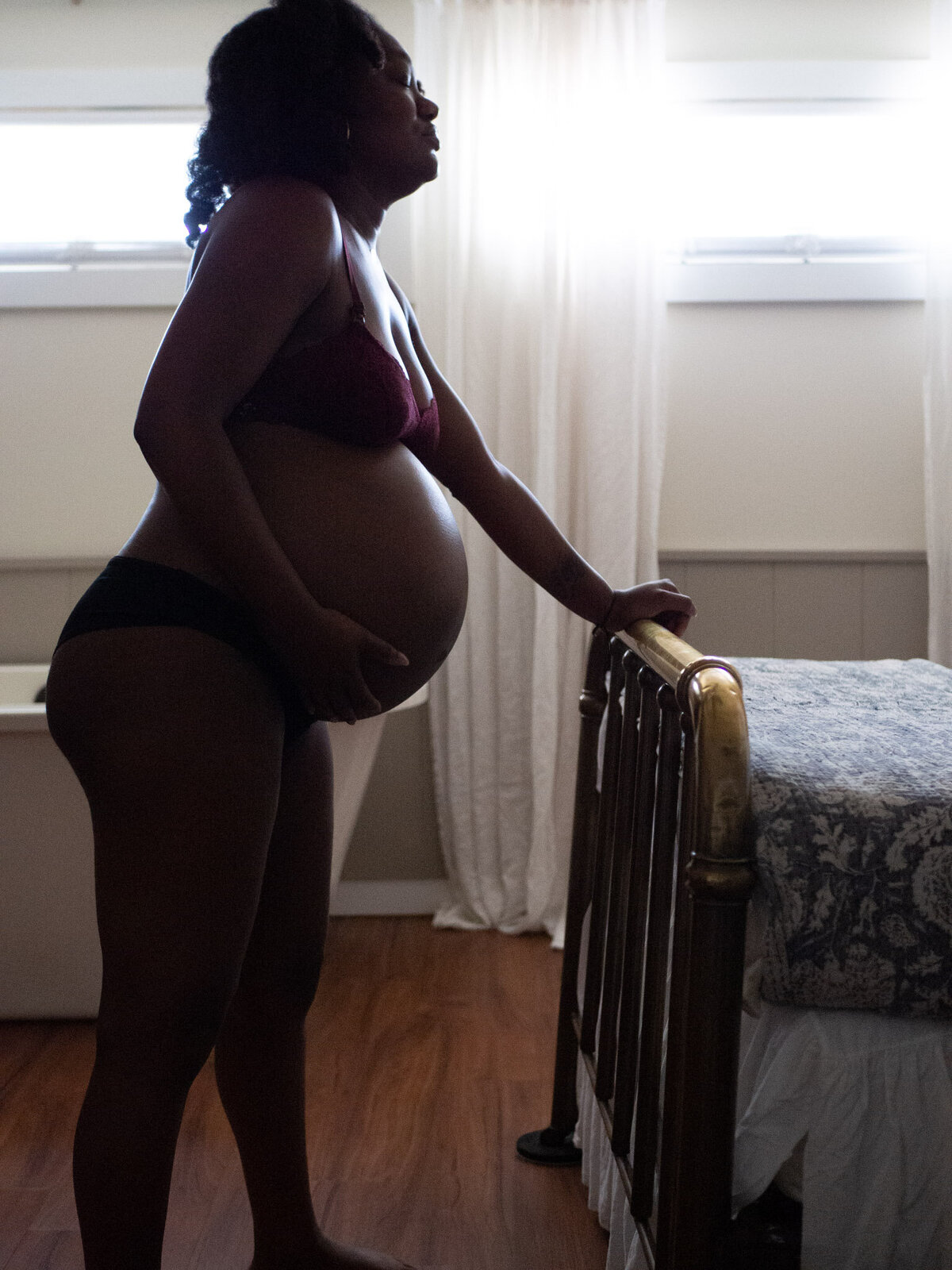 An African American pregnant woman is holding her belly as she labors standing while holding  a bed rail at a birthing center in Seattle, WA.
