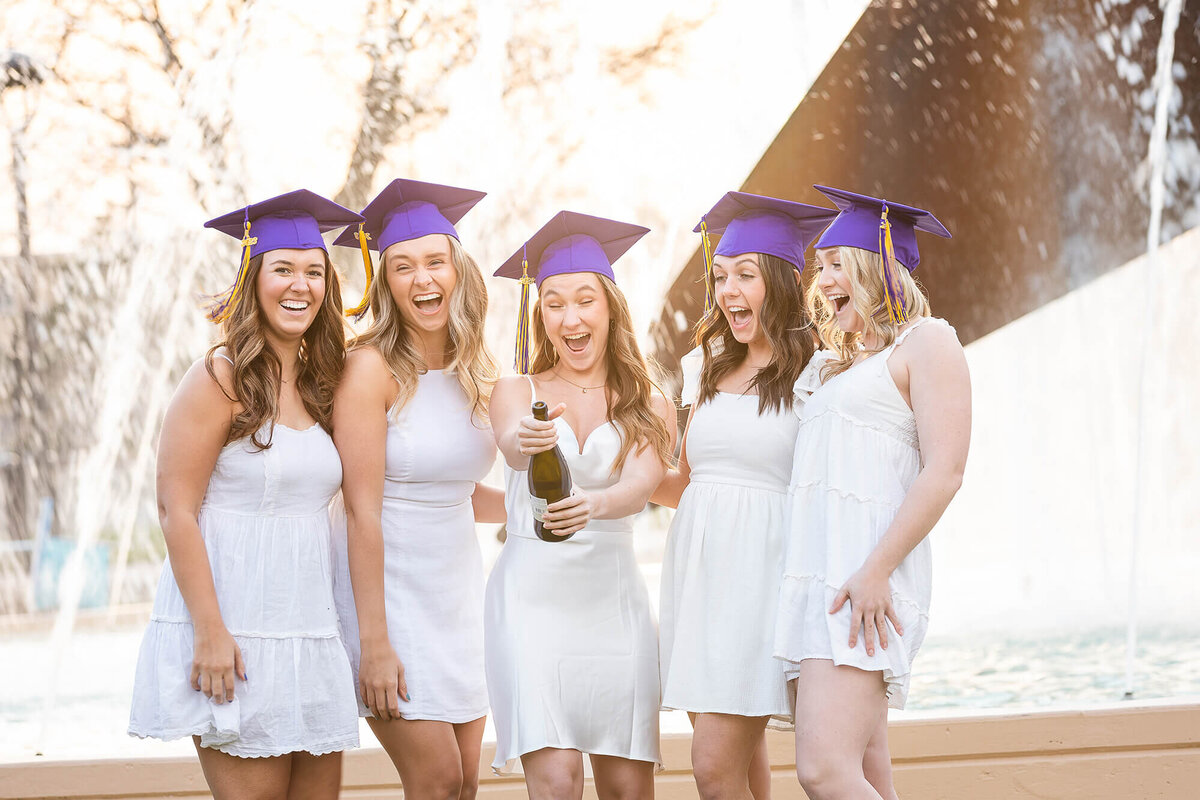 Five girls celebrating college graduation with a bottle of champagne.