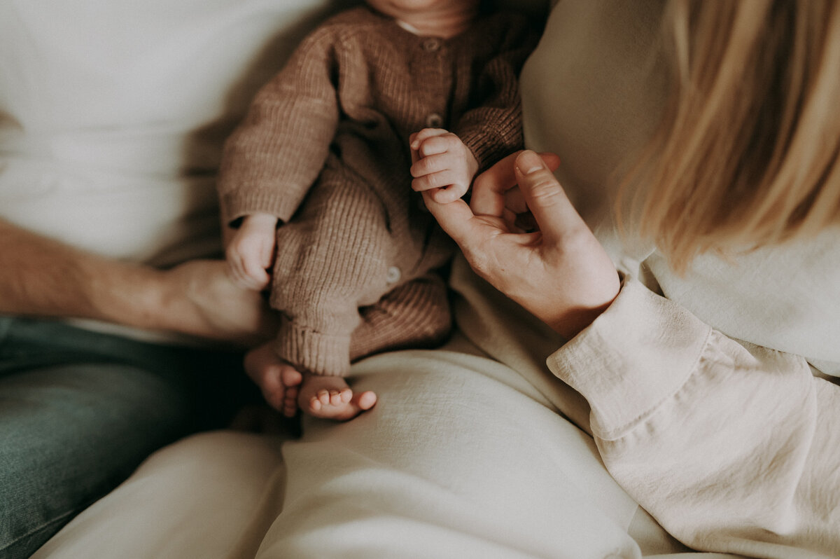 Newborn baby zit bij zijn ouders op de schoot. Detail van handen.