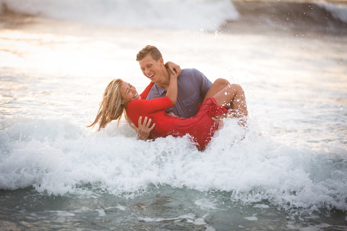 Groom to be carries his Bride in the ocean waters as the waves crash down all around them