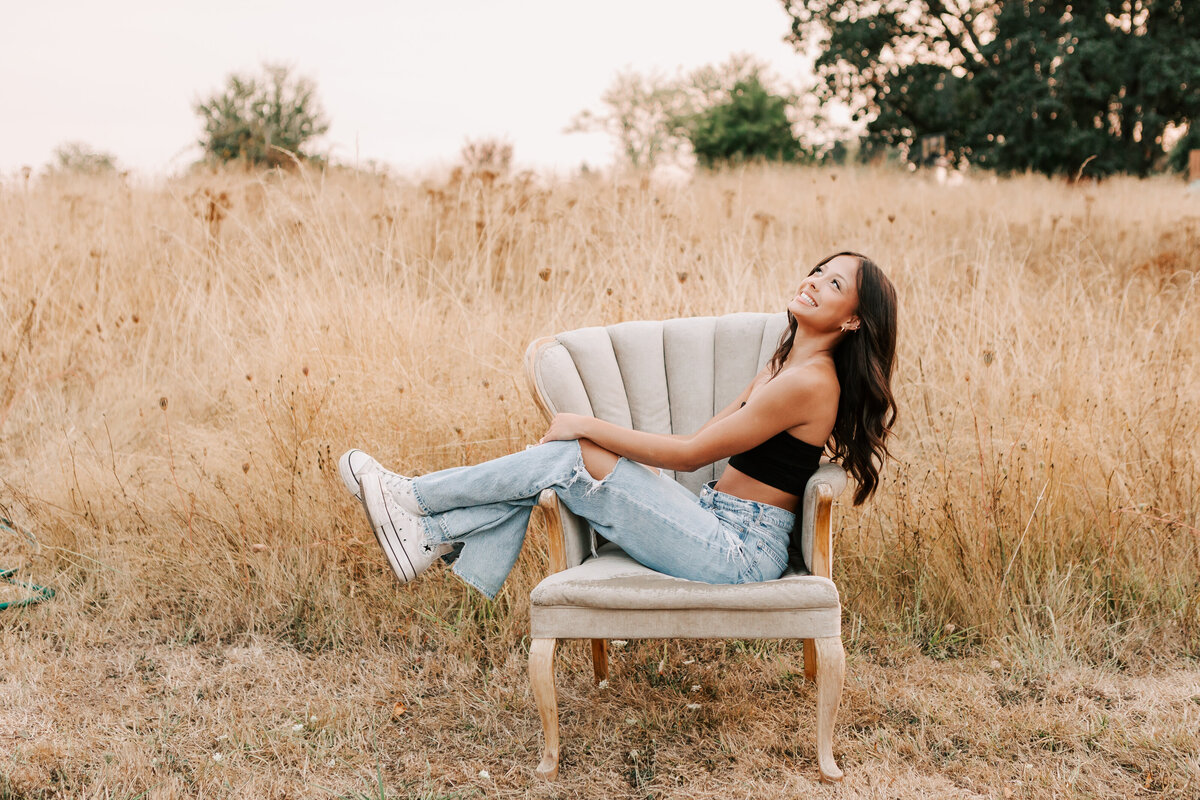 A girl in jeans and a black top sits on a chair smiling at a farm in Albany, Oregon