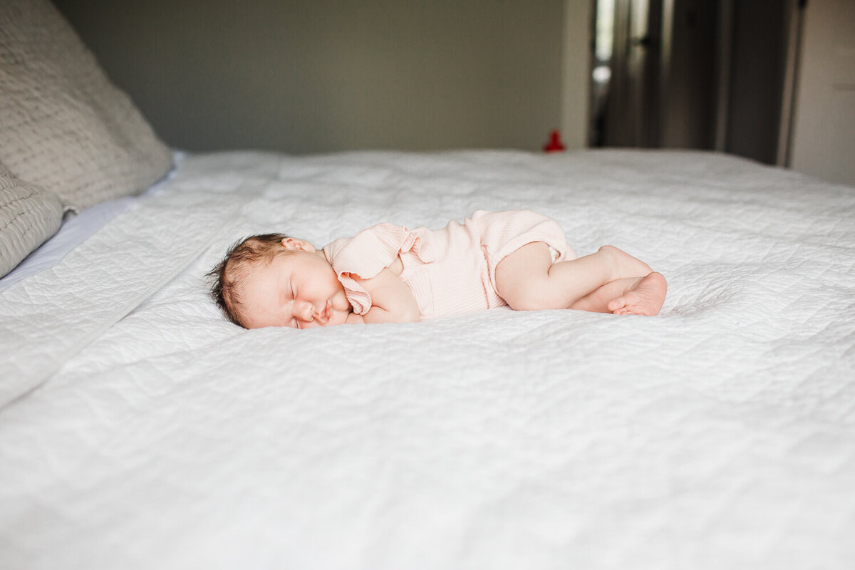 newborn girl in pink onesie sleeping on bed