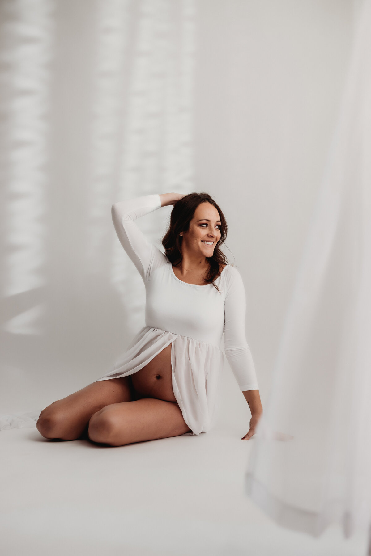 pregnant mom lays on white floor in a long green dress with bare belly exposed for maternity photos