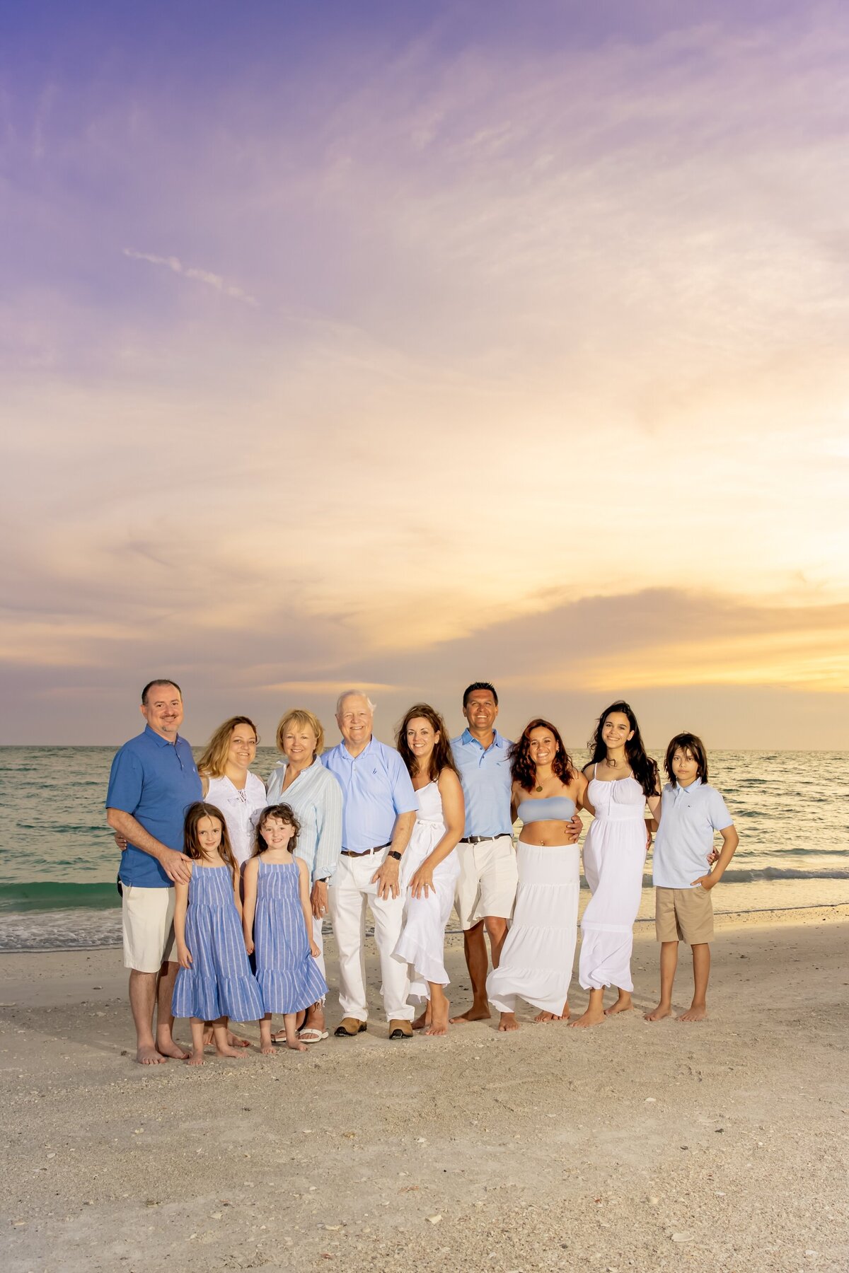 A family dresses up for holiday photos on  the beach with a pastel sunset.