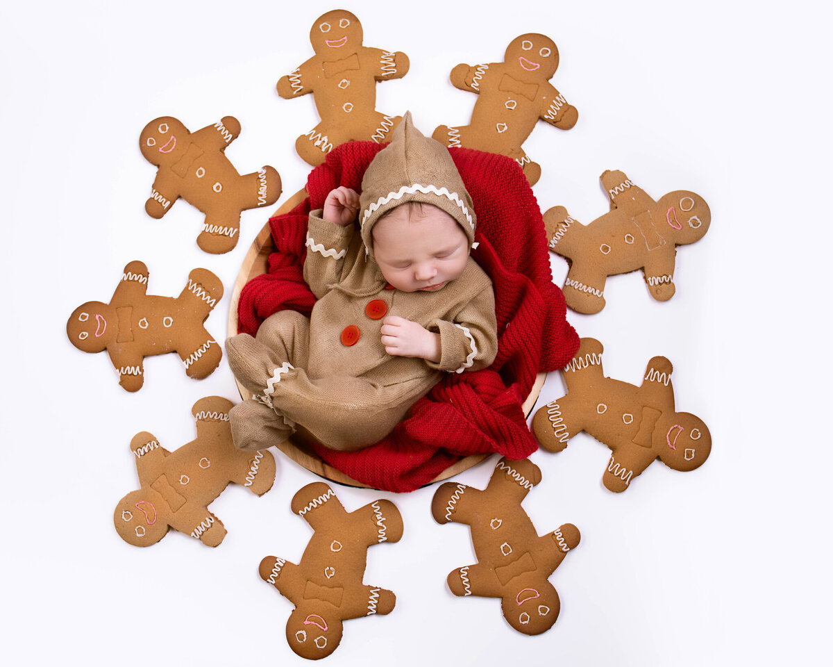 Newborn nestled in a gingerbread-inspired setup, surrounded by holiday cookies, captured in Overland Park, Kansas. A delightful holiday theme for families seeking festive newborn photography.