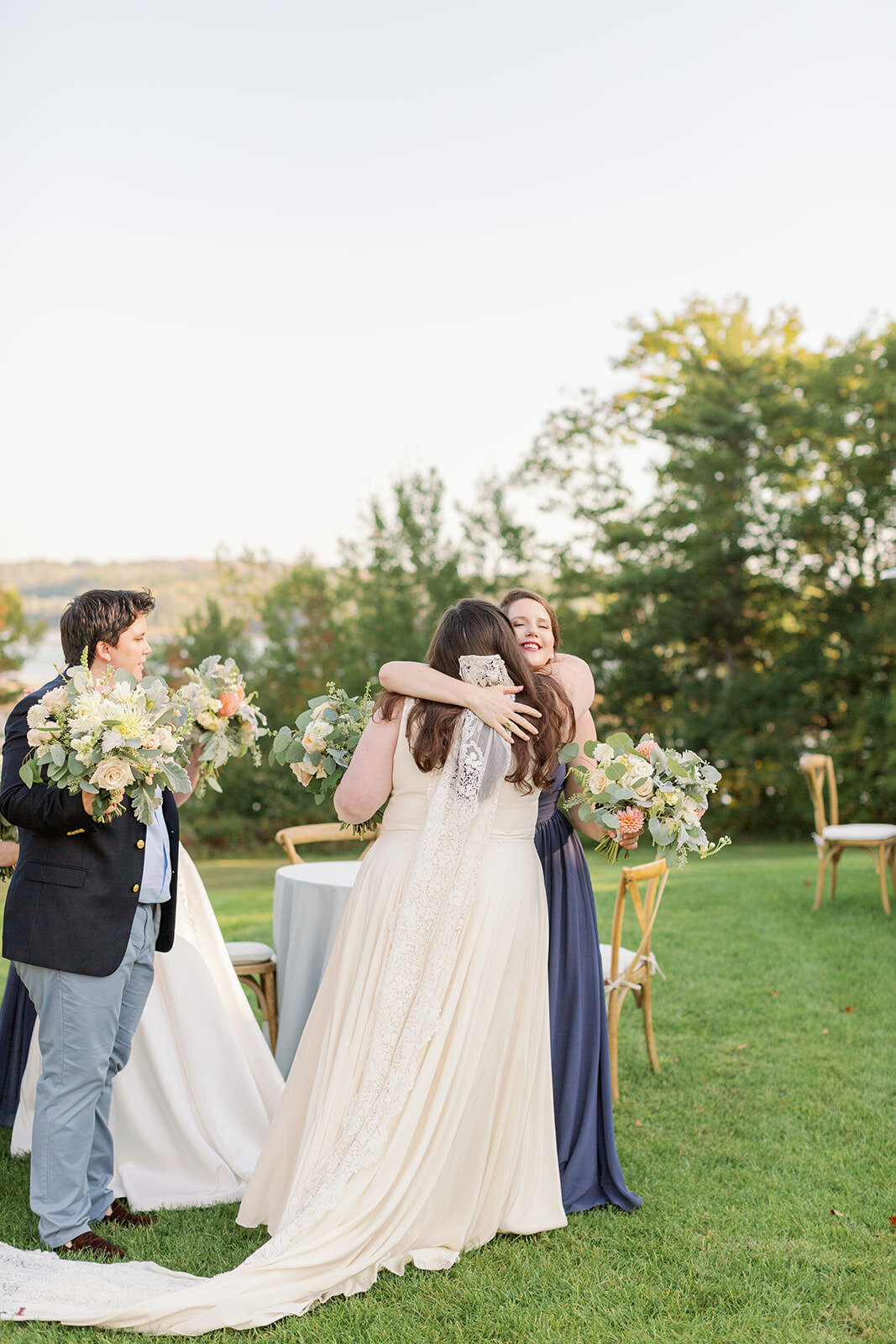 A bride hugging someone as another person stands next to them with a bouquet of flowers.