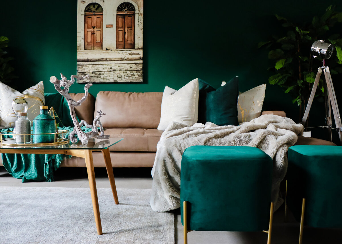 Dark green painted walls create a boho loung with a tan leather sofa and a beige throw.